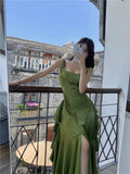 Woman in olive green satin maxi dress with ruffles and thigh slit, taking mirror selfie on balcony