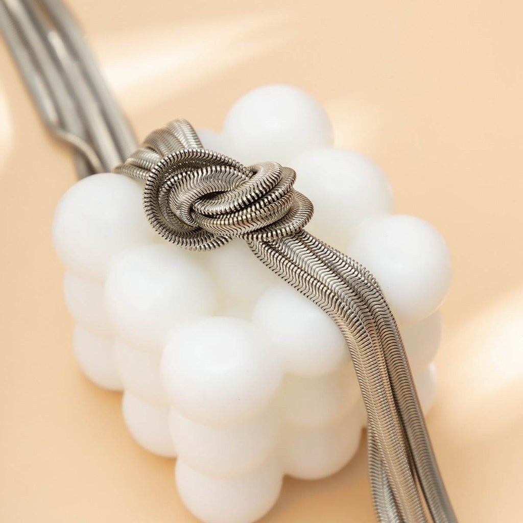 Elegant silver mesh hair tie with knotted design, styled on white spherical beads for chic everyday wear.