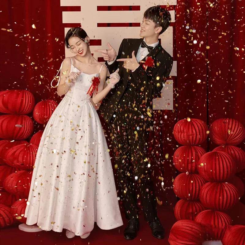 Couple in wedding attire celebrating with confetti and red lanterns, elegant bridal gown and tuxedo