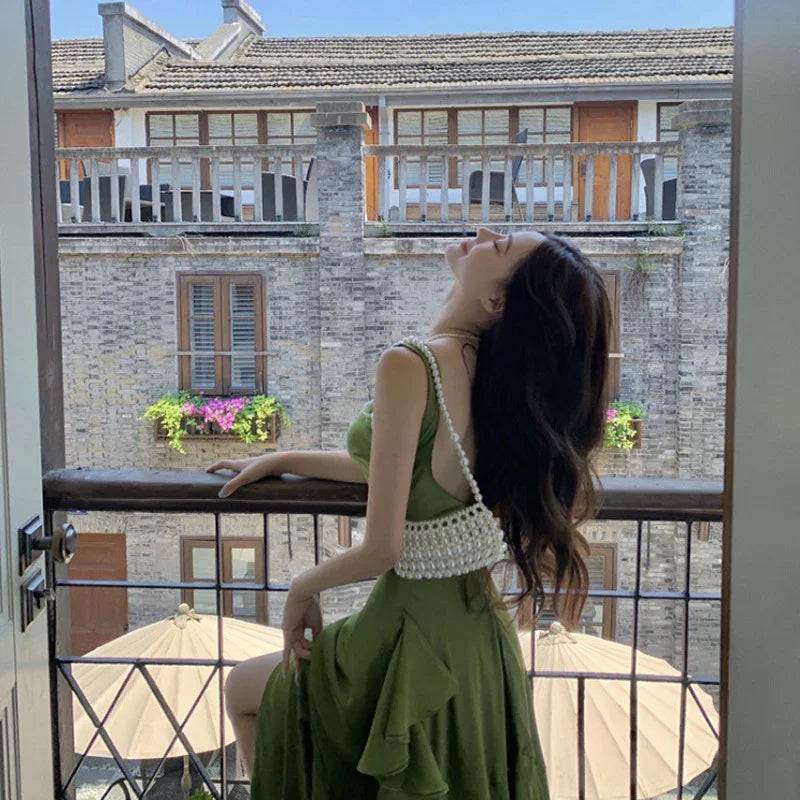Woman in olive green maxi dress with pearl strap, relaxing on balcony with vintage building view