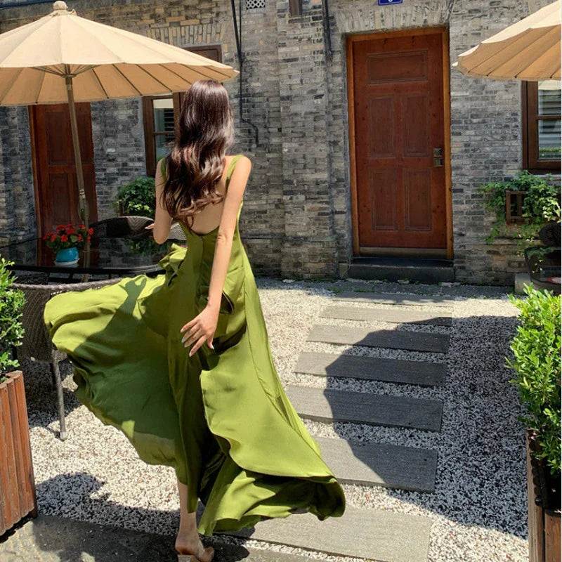 Woman in flowing olive green maxi dress twirling outdoors near stone building