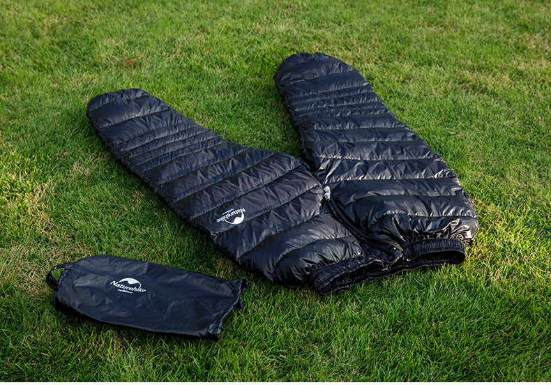 Laylace black goose down puffer pants with matching storage bag laid out on green grass for outdoor camping