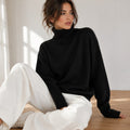 Laylace black knitted turtleneck sweater with long sleeves worn by a woman sitting on a wooden floor