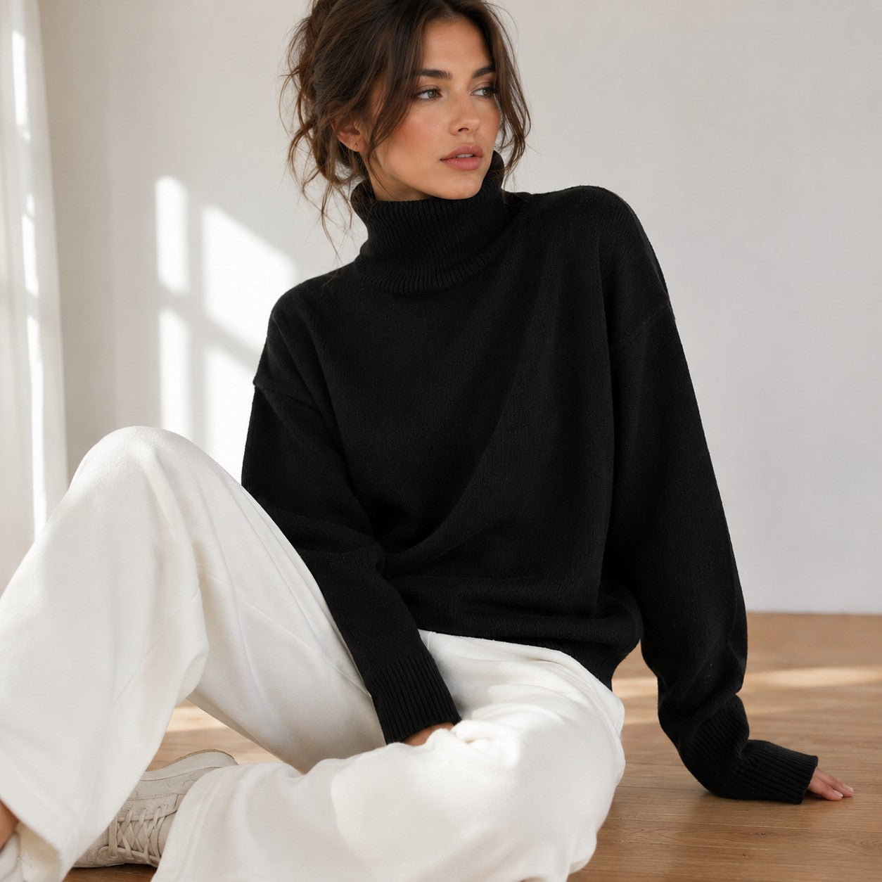 Laylace black knitted turtleneck sweater with long sleeves worn by a woman sitting on a wooden floor