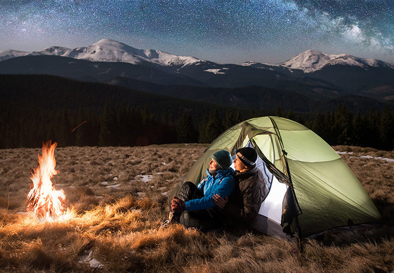 Laylace goose down puffer pants worn by a couple camping by a campfire under a starry mountain sky