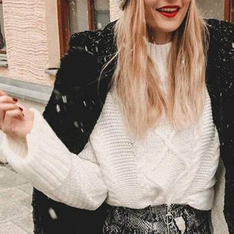 Laylace white cable knit sweater with a round neck worn by a woman under a black coat in a snowy outdoor setting