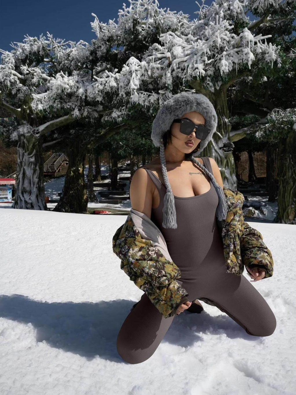 Woman in ribbed bodysuit and floral puffer jacket posing in snowy landscape with fur hat