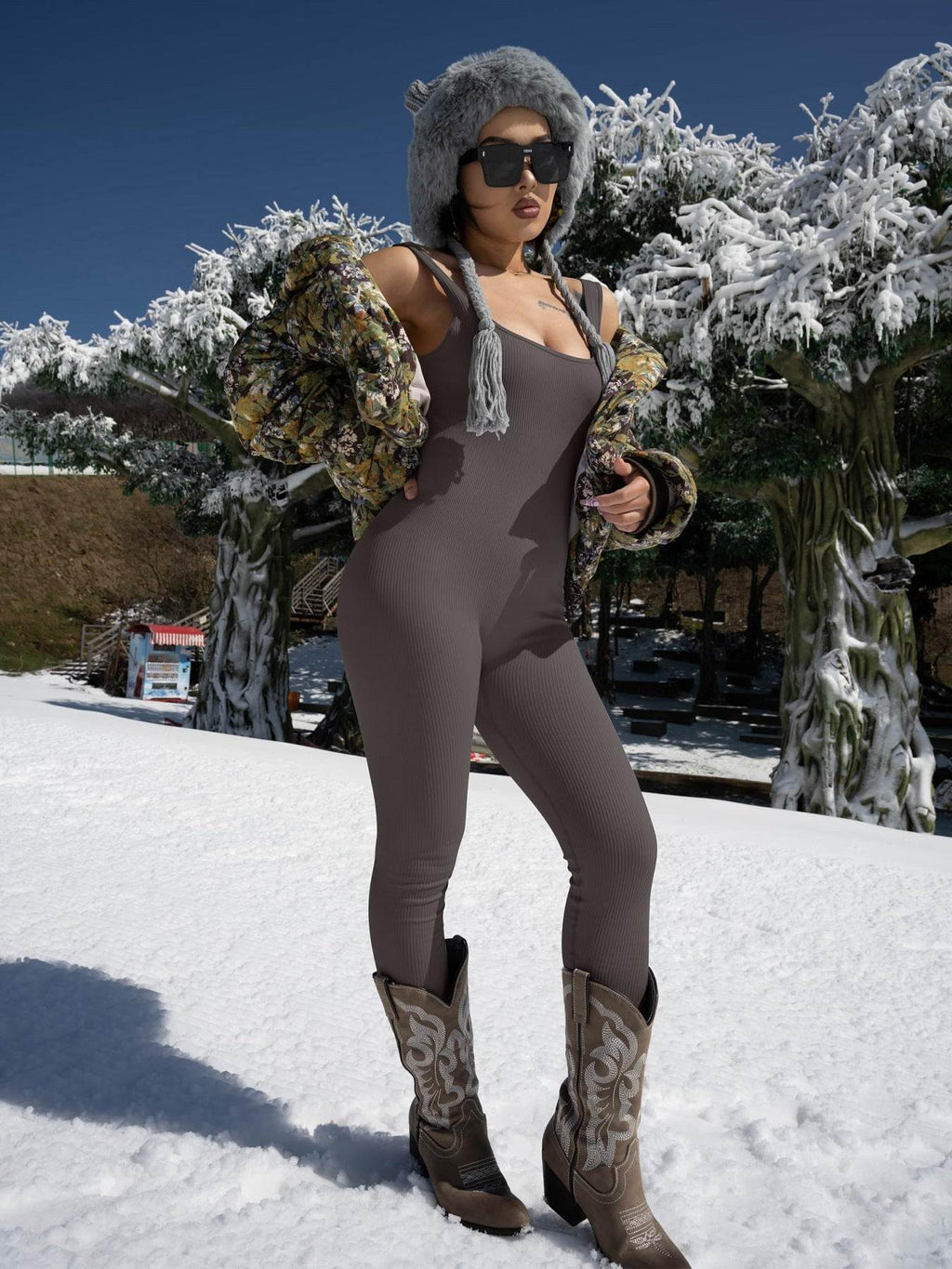Woman in ribbed bodysuit, floral jacket, and cowboy boots posing in snowy landscape with fur hat