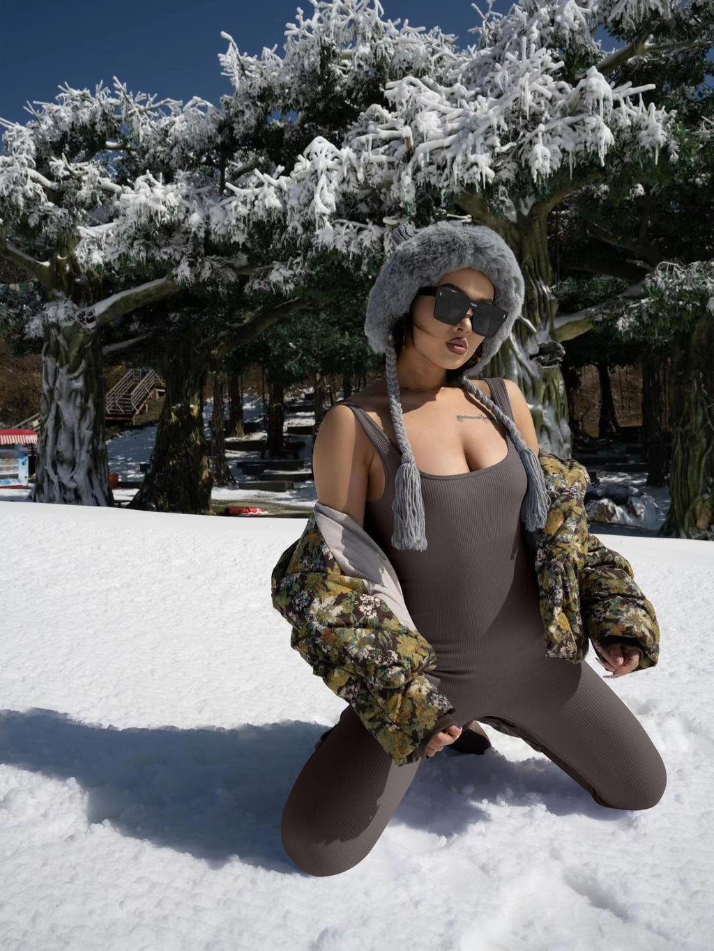Woman in ribbed bodysuit and floral puffer jacket posing in snowy landscape with fur hat