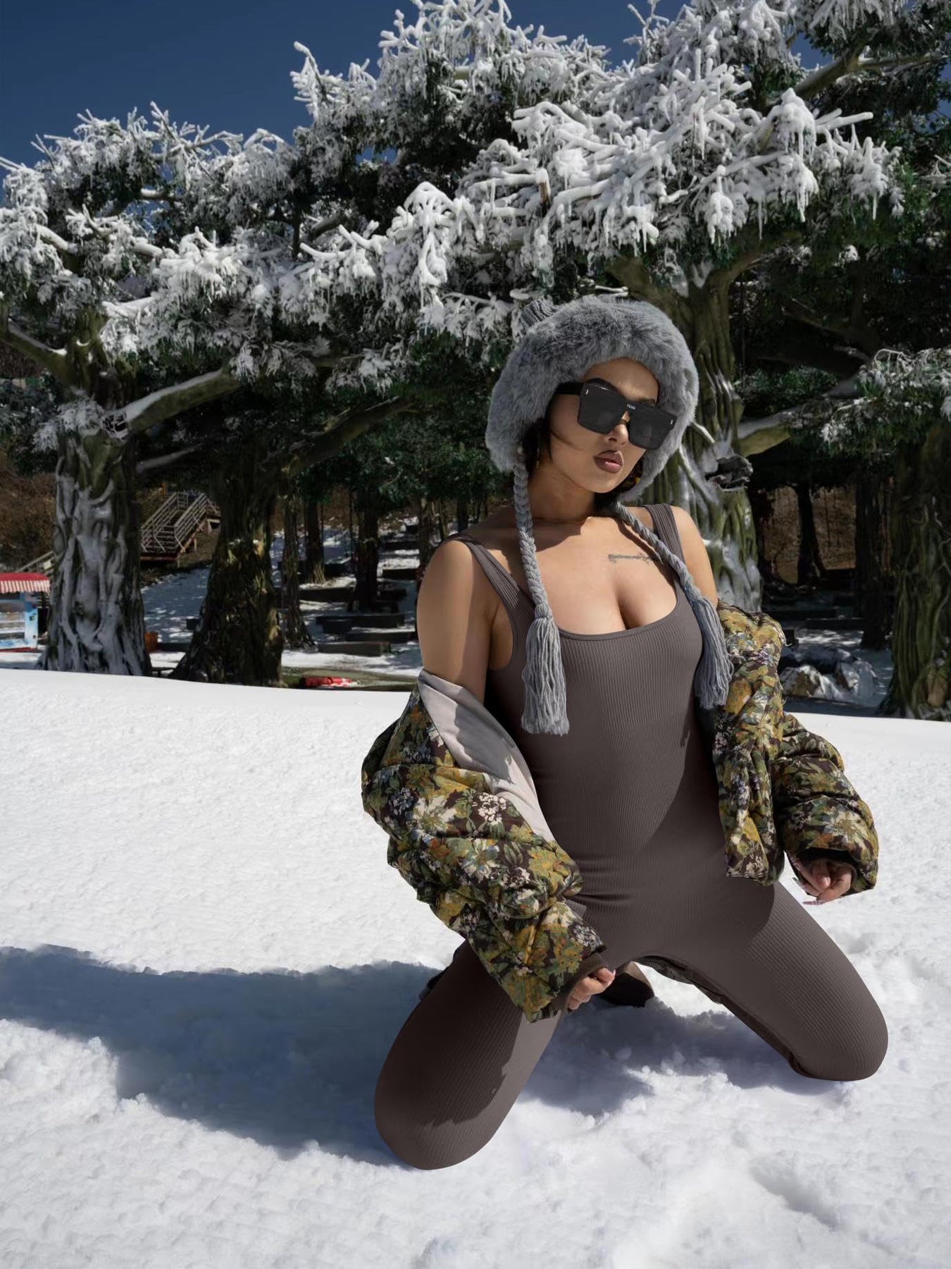 Woman in ribbed bodysuit and floral puffer jacket posing in snowy landscape with fur hat