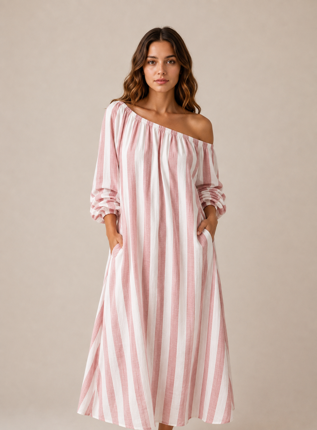A woman modeling a pink and white vertically striped off-the-shoulder maxi dress with long ruffled sleeves and side pockets, set against a solid beige studio background.