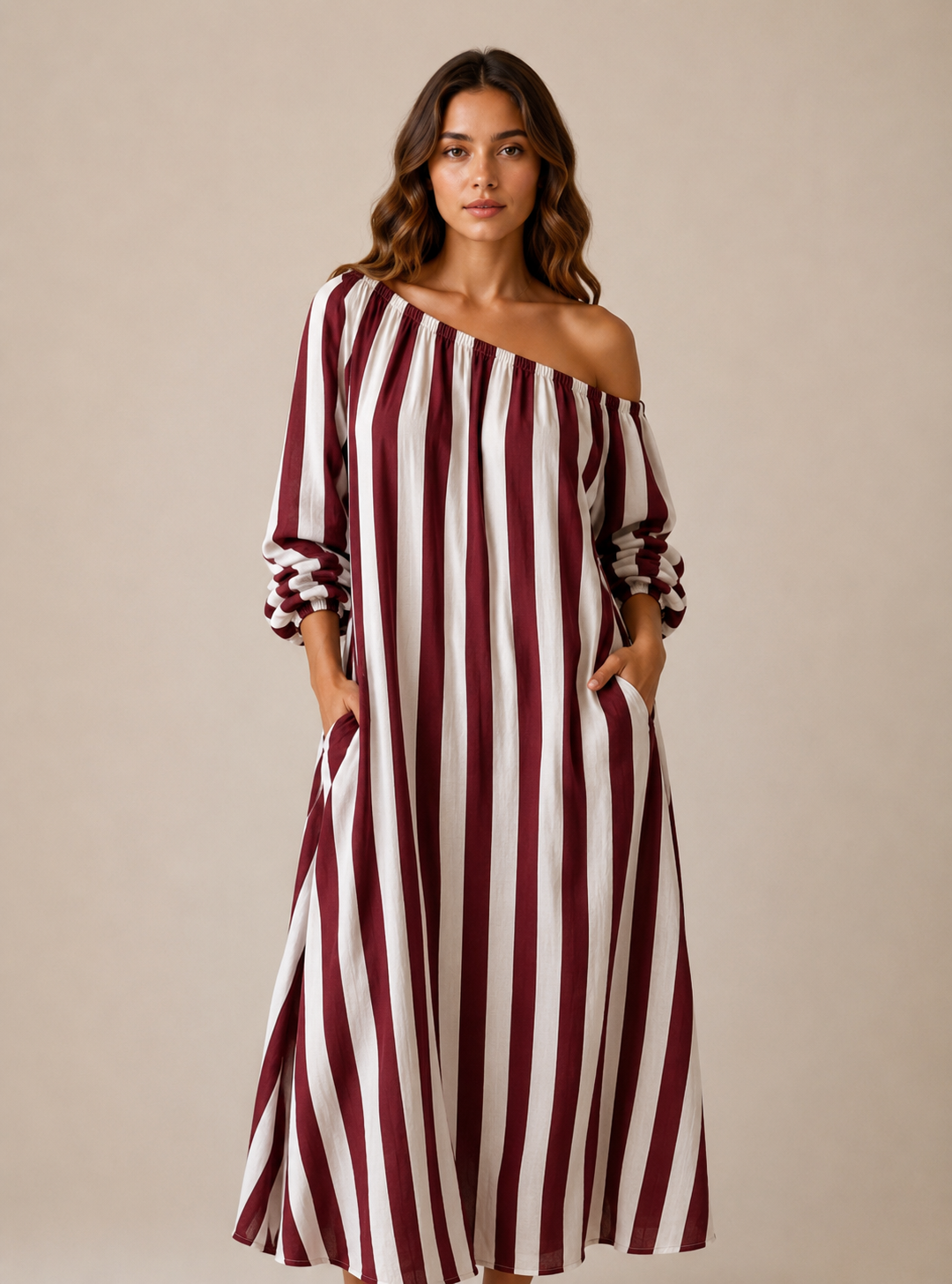 A woman modeling a long off-the-shoulder maxi dress with vertical burgundy and off-white stripes, standing against a plain beige studio background.
